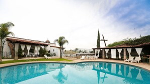 A swimming pool with white chairs and umbrellas, surrounded by buildings with tiled roofs and white walls. - Posada la Ermita (San Miguel de Allende)
