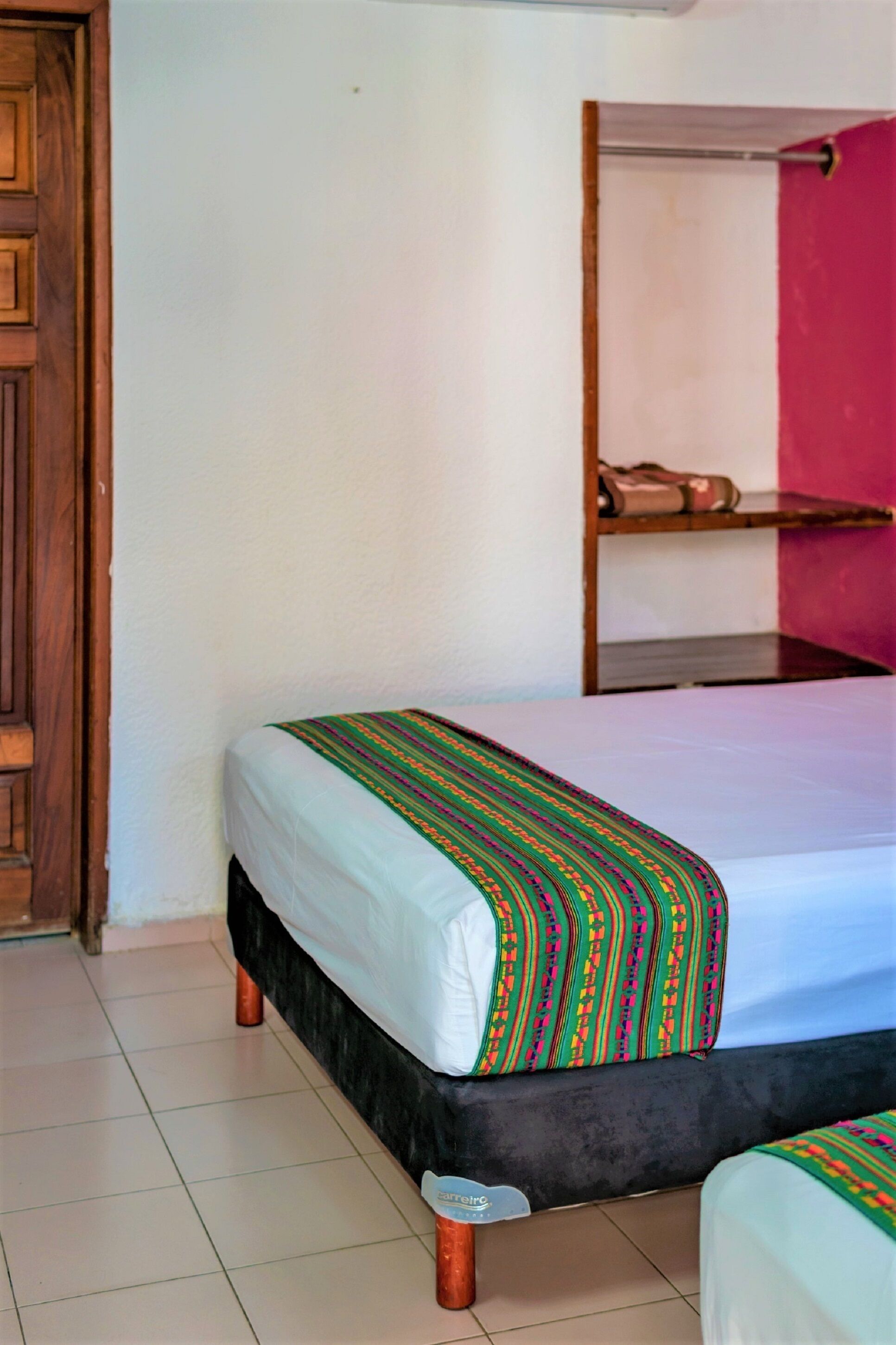A hotel room with two beds, a wooden door, a tiled floor, and a pink curtain.