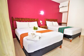 Une chambre d’hôtel avec deux lits, une tête de lit en bois, du linge de lit blanc, un plaid orange, une petite plante en pot et une table de chevet avec une lampe.