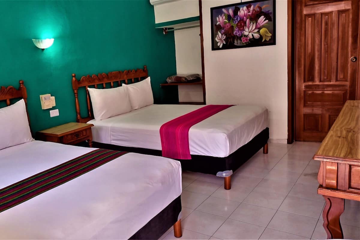 A hotel room with two beds, a wooden headboard, a nightstand, a wall-mounted light, a painting, and a wooden door.