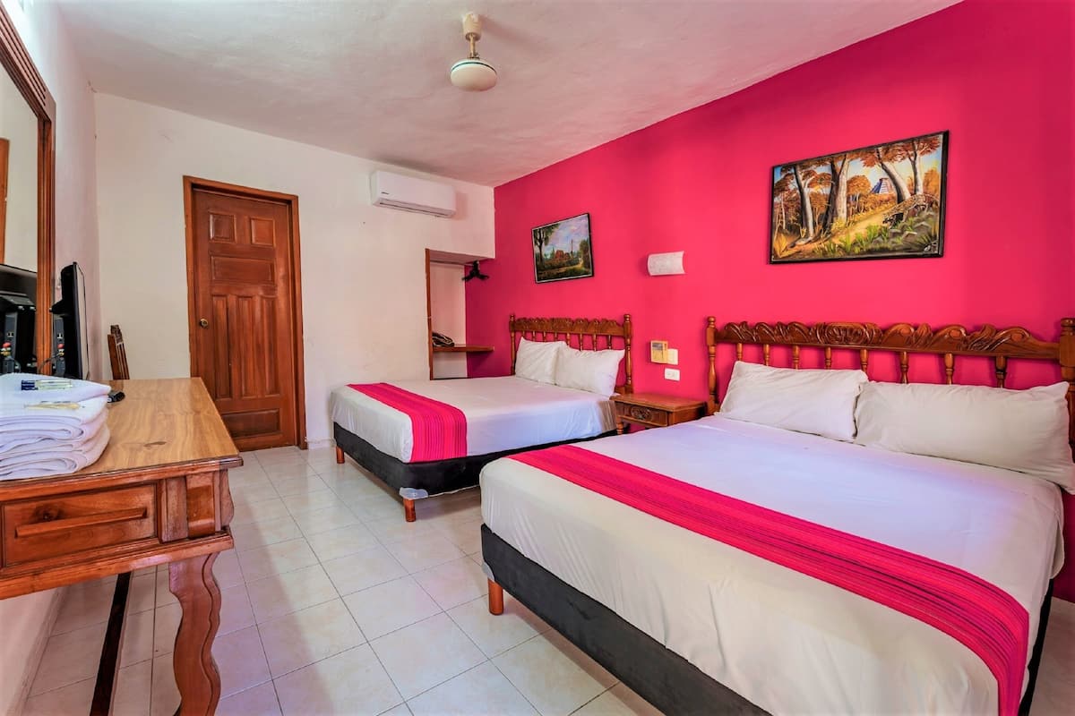 A hotel room with two beds, a wooden desk, a chair, and a painting on the wall.
