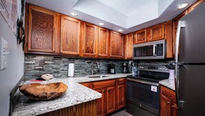 Una cocina con armarios de madera, encimera de granito, refrigerador de acero inoxidable y microondas integrado.