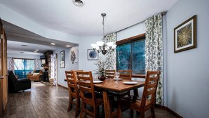 Comedor con mesa y sillas de madera, un candelabro y una ventana con vista a árboles.