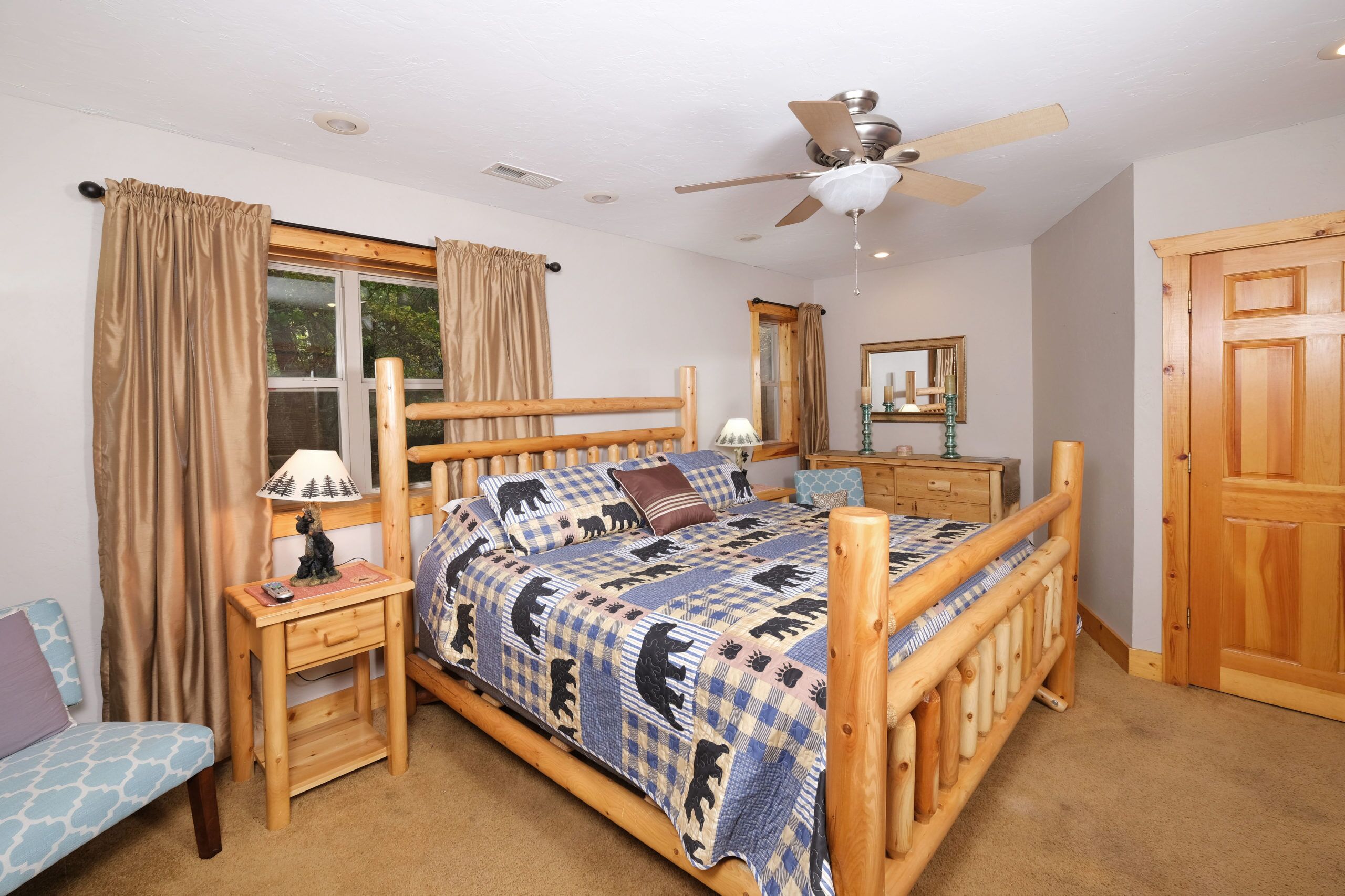 A wooden four-poster bed with a checkered blanket, a bedside table with a lamp, a nightstand, and a chair.