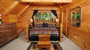 Une chambre dans une cabane en bois, avec un lit, des tables de chevet, une commode, un miroir et une fenêtre avec des rideaux.