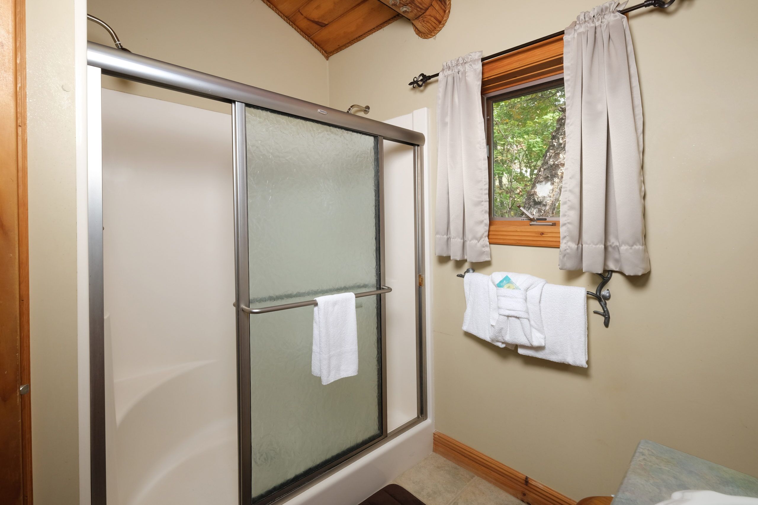 A shower with a glass door, a window with curtains, and a towel rack with towels.