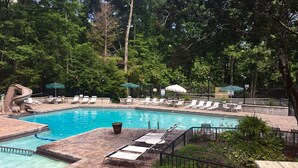 Une piscine rectangulaire avec un toboggan, entourée de chaises longues et de parasols, située dans un espace boisé.
