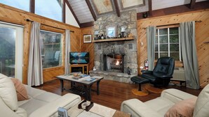 A cozy living room with a stone fireplace, wooden walls, a television, and comfortable seating.