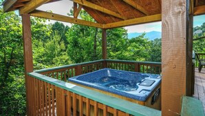 A hot tub in a wooden gazebo with a view of a forested area.