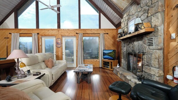 A cozy living room with a stone fireplace, wooden beams, and a large window overlooking a scenic landscape.