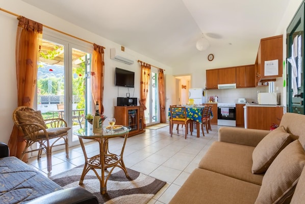 Ein modernes Wohnzimmer mit Sofa, Esstisch mit Stühlen, Fernseher und Küchenzeile mit Holzschränken und Kühlschrank.