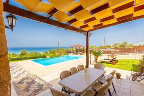 A covered outdoor area with a pool, a table with chairs, and a view of the sea. - Villa Minoas - Four Bedroom Villa, Sleeps 10 (Argaka)