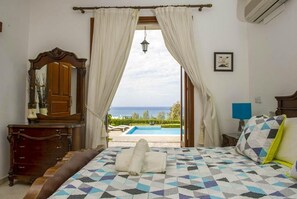 Ein Schlafzimmer mit Bett, Schminktisch, Spiegel und Blick auf einen Pool.