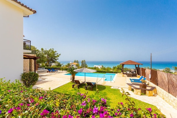 A pool area with a view of the sea, a gazebo, and a well-maintained lawn with flowers. - Villa Minoas - Four Bedroom Villa, Sleeps 10 (Argaka)