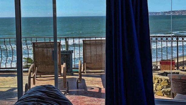 A balcony with a view of the ocean, two chairs, and a table.