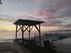 Un belvédère en bois avec des tables de pique-nique, offrant une vue sur un plan d’eau au coucher du soleil.