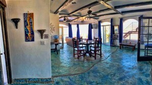 A spacious room with a blue floor, a dining area with chairs and a table, and large windows with curtains.