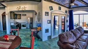 A spacious living area with a leather sofa, a dining table, and a kitchen in the background.
