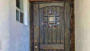 A wooden door with a metal grid lock, set in a hallway with a white wall and a small window above it.