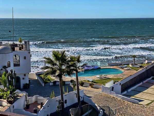 Un hôtel en bord de mer doté d’une piscine, de palmiers et offrant une vue sur l’océan.