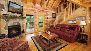 Interior acogedor de una cabaña con chimenea de piedra, un sofá de cuero rojo, una mesa de centro de madera y una escalera.