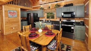 Cocina tipo cabaña de madera con una mesa de comedor preparada para cuatro personas, equipada con refrigerador, estufa y microondas.