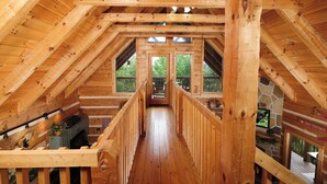 Un interior de madera con techo alto, vigas de madera, una escalera central y una pared de piedra con un televisor.