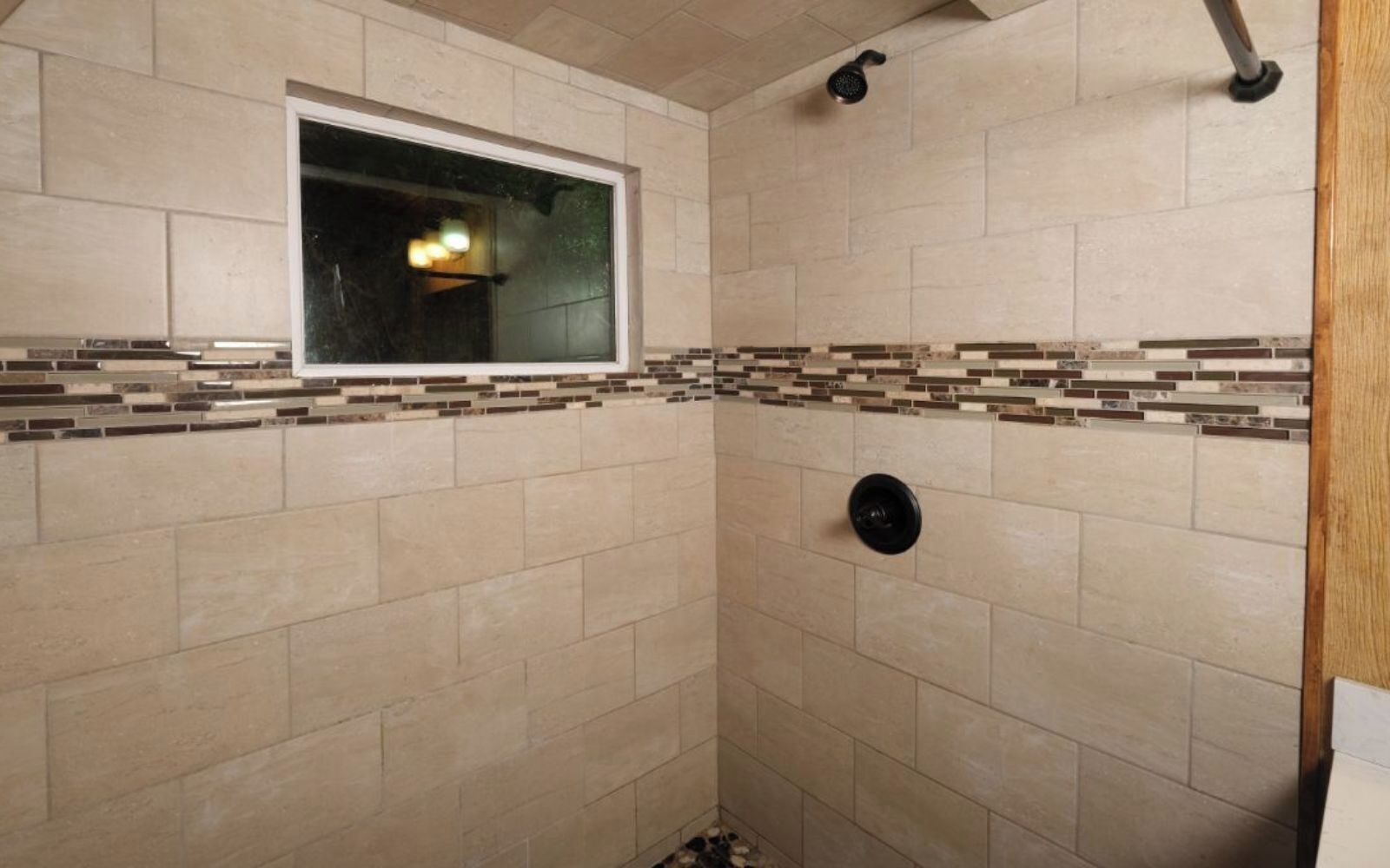 Ducha con azulejos color beige, una ventana y un cabezal de ducha.