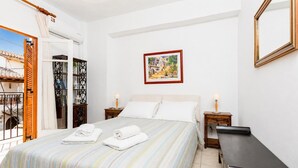 Una camera d'albergo con un letto, due comodini, un tavolino, una finestra con tende e un quadro appeso al muro.