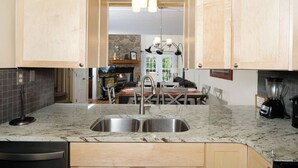 A kitchen with granite countertops, a stainless steel sink, wooden cabinets, a dining area with a table and chairs, and a stone fireplace. - Three Bears and a Mountain HA302 - Community - Fireplace - Mountain Views (Gatlinburg)