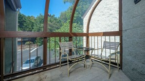 A sunroom with a view of a road and trees. It has two chairs and a small table. - Three Bears and a Mountain HA302 - Community - Fireplace - Mountain Views (Gatlinburg)