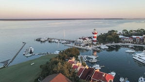 A marina with boats docked, a lighthouse, and buildings with red roofs.