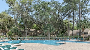 A pool area with lounge chairs and a clear blue pool surrounded by trees.