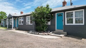 A row of single-story houses with grey exteriors and blue doors, each with a small front porch and a tree in front.