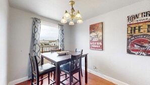 A dining area with a wooden table, four chairs, a chandelier, and two posters on the wall.