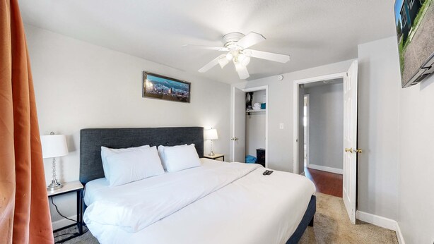 A hotel room with a bed, a ceiling fan, a nightstand with a lamp, and a door leading to another room.