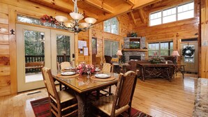 A spacious wooden cabin with a dining area, fireplace, and large windows. - Hemlock Ridge 1713 - Mountain View from Hot Tub (Gatlinburg)