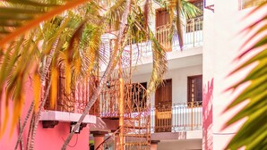 A pool area with a fountain, surrounded by potted plants and palm trees, with a pink building in the background. - Hotel Santa Lucía (Mérida)