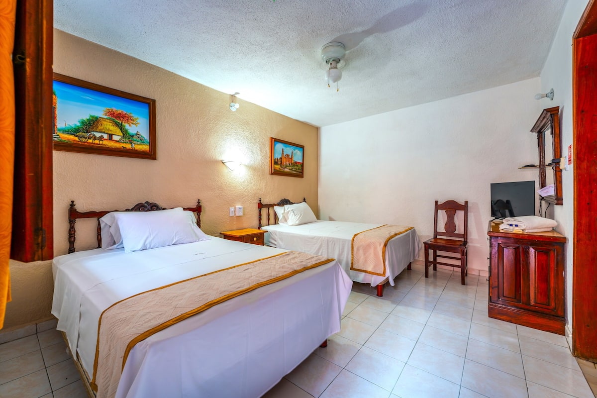A hotel room with two beds, a wooden cabinet, a chair, and two wall-mounted paintings.