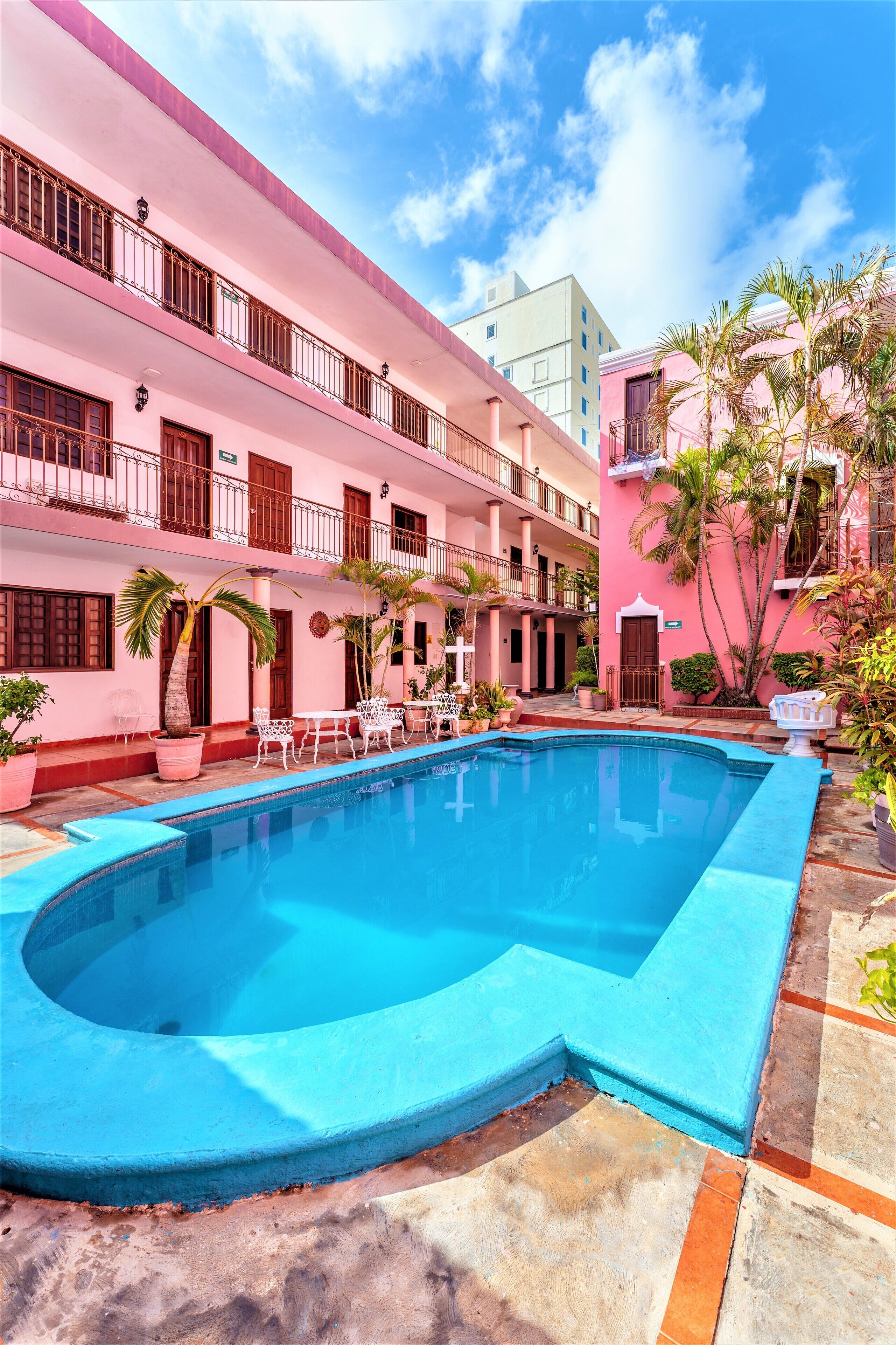 A pink building with a swimming pool, outdoor seating, and palm trees.