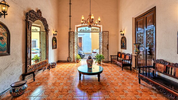A lobby with a tiled floor, a central table with a vase, a chandelier, and a sign reading "HOTEL". - Hotel Santa Lucía (Mérida)