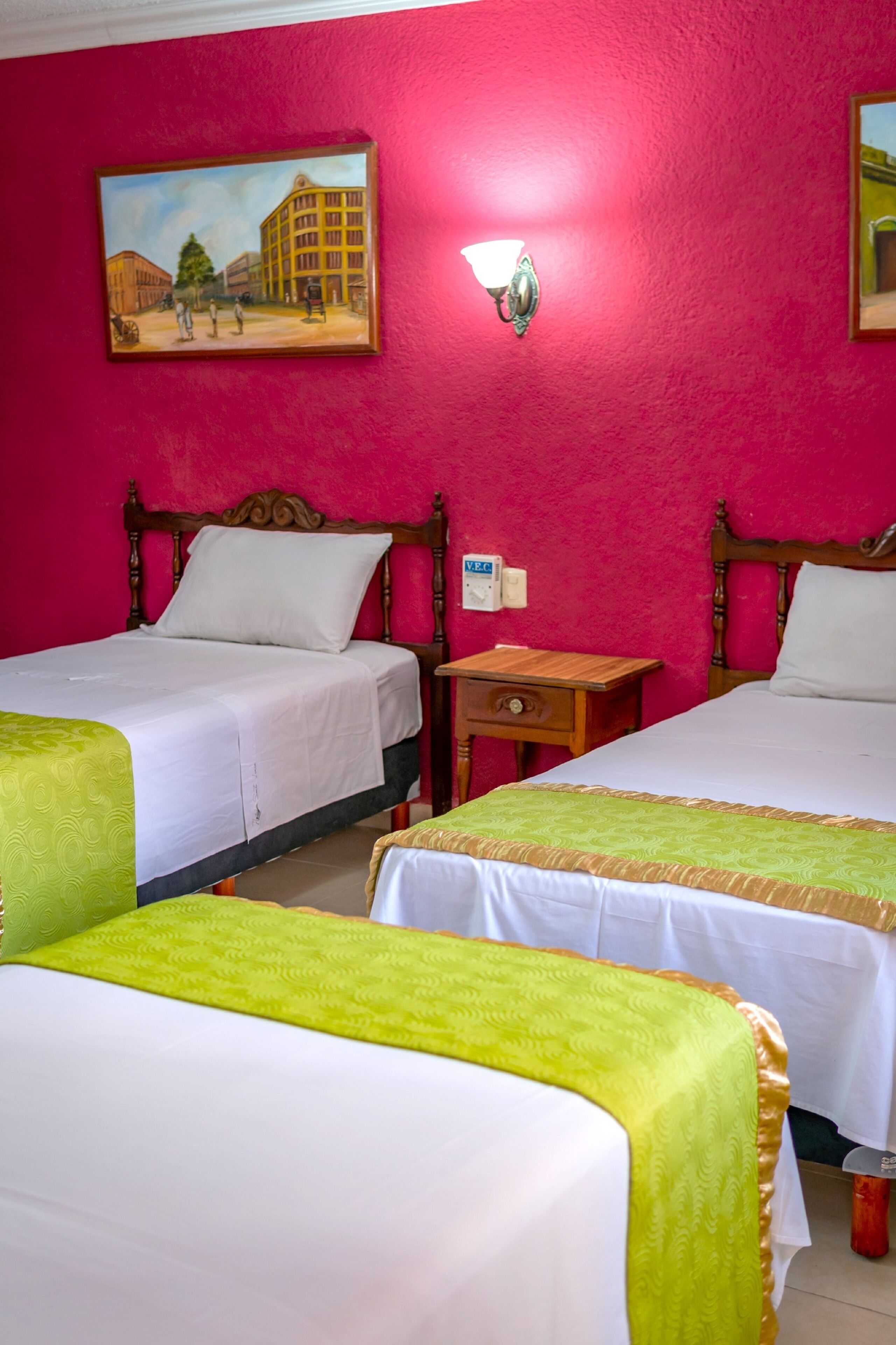 Ein Hotelzimmer mit zwei Einzelbetten, einem hölzernen Kopfteil, einem Nachttisch, einem Bild an der Wand und einer Wandleuchte.