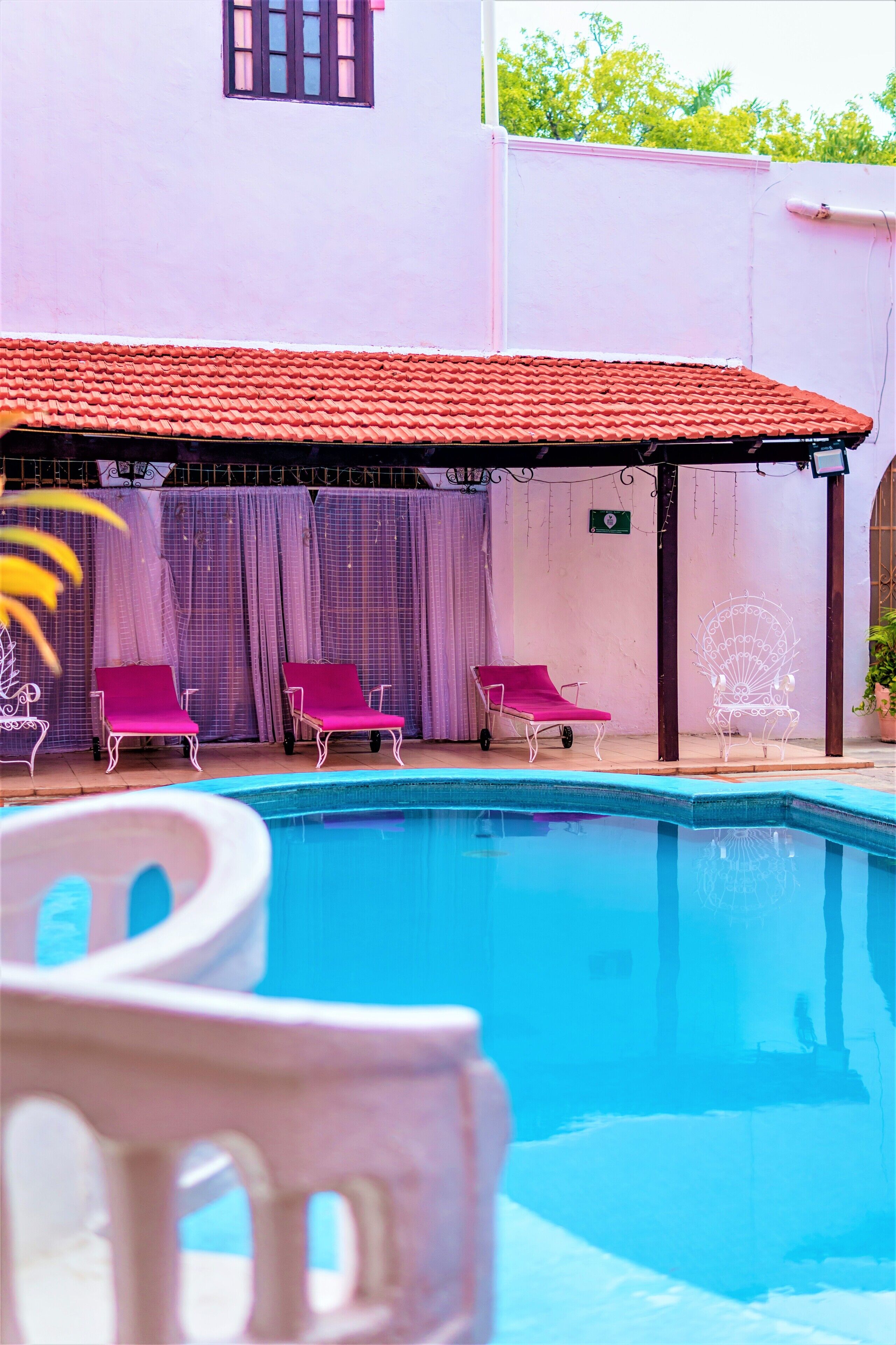 Una piscina con techo de tejas rojas, rodeada de sillas blancas y un área techada.