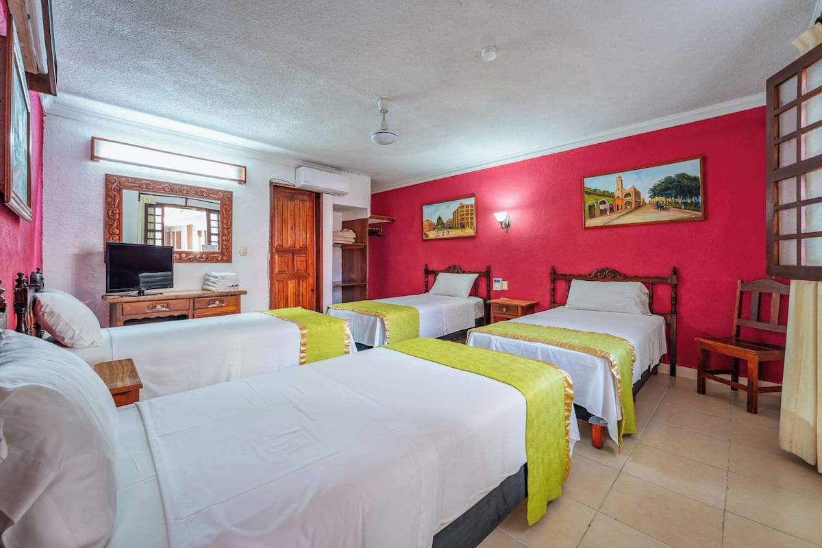 A hotel room with four beds, a television, a mirror, and two paintings on the walls.