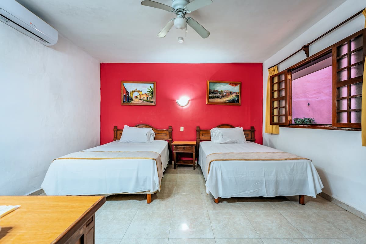 A room with two beds, a ceiling fan, and a window with curtains.