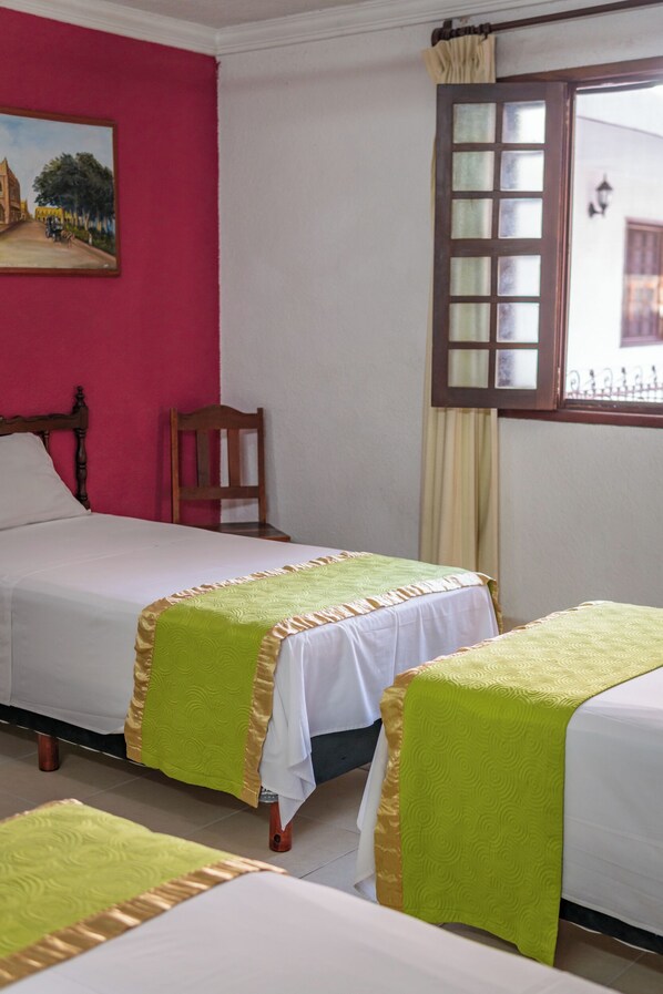 Una habitación de hotel con dos camas, una silla de madera, un cuadro en la pared y una ventana con cortinas.