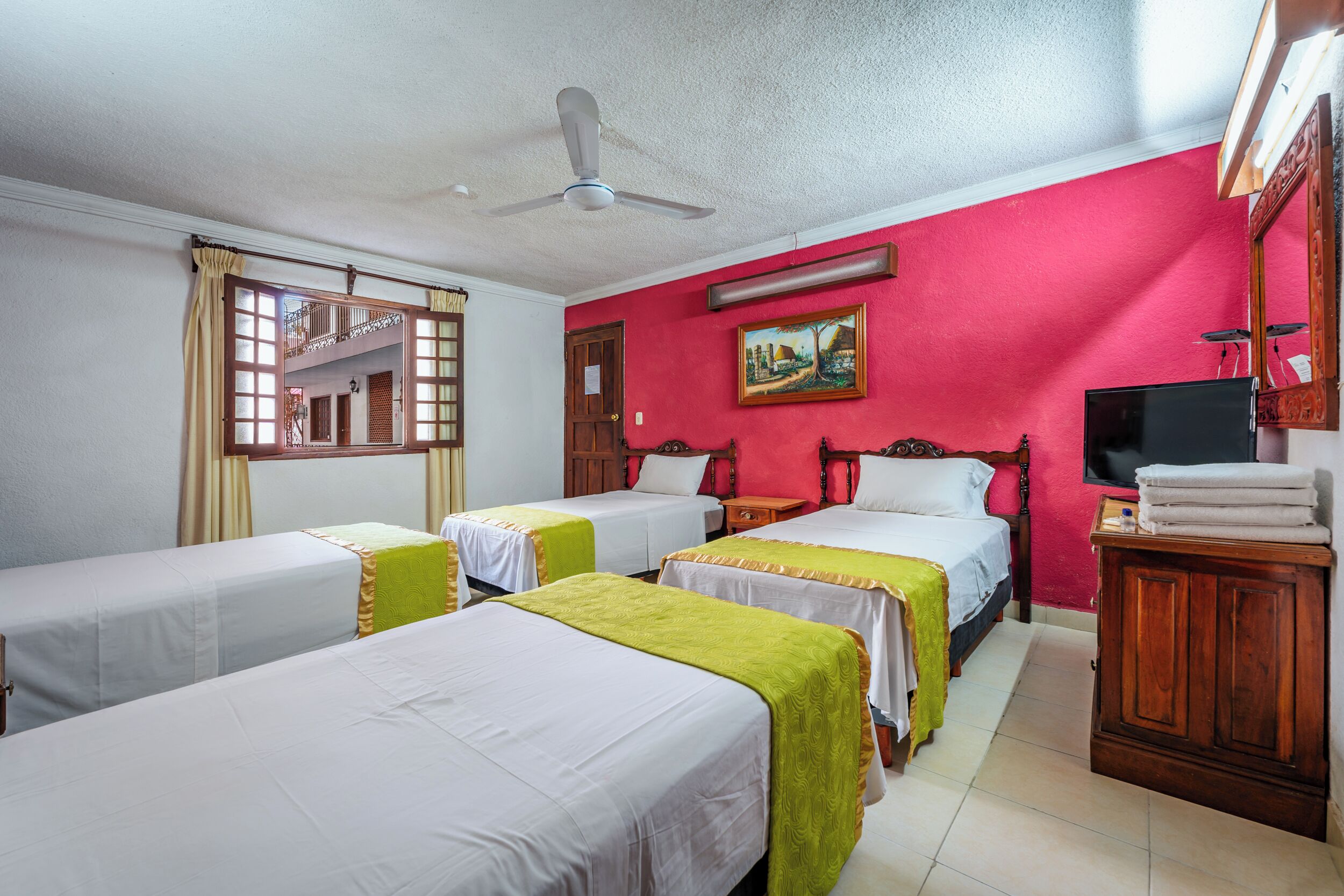 A hotel room with three single beds, a ceiling fan, a TV, and a wooden cabinet.