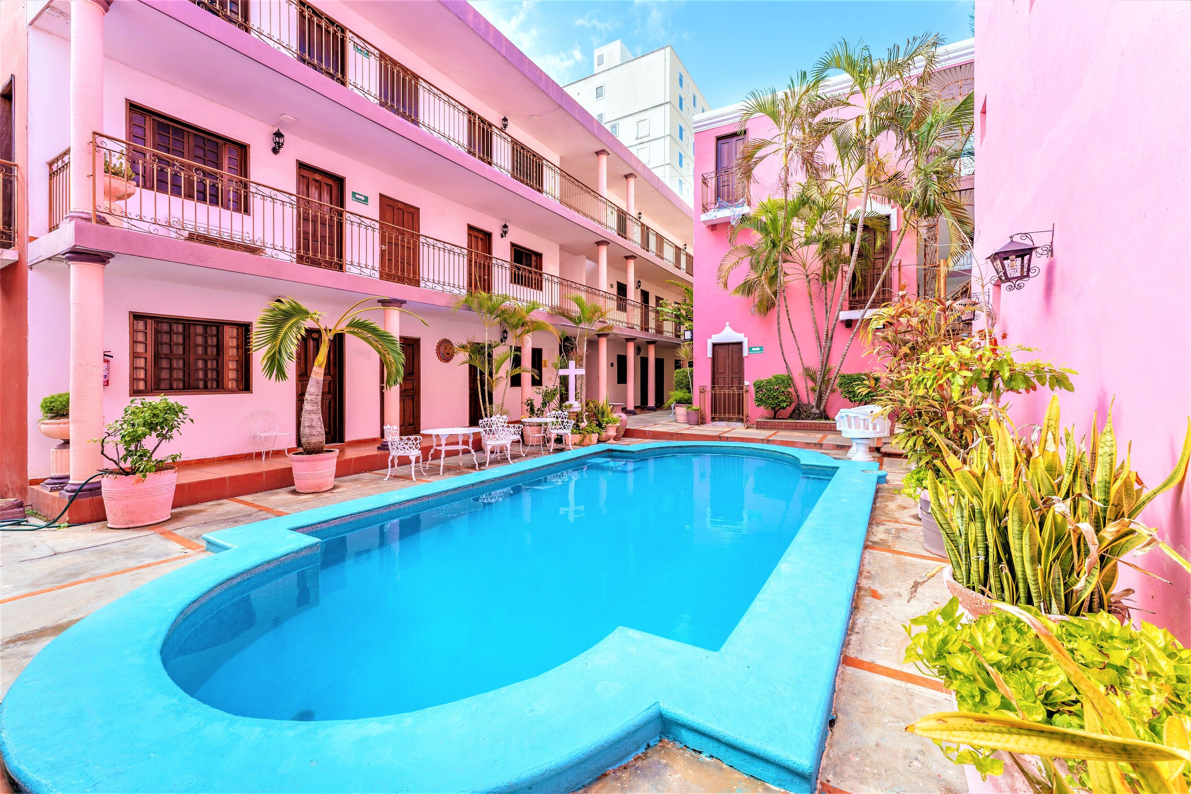 A pink building with a swimming pool, potted plants, and outdoor furniture.