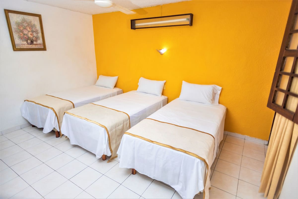A hotel room with three single beds, white bedding, and a yellow accent wall.