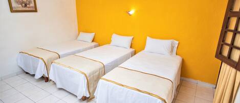 A hotel room with three single beds, white bedding, and a yellow accent wall.